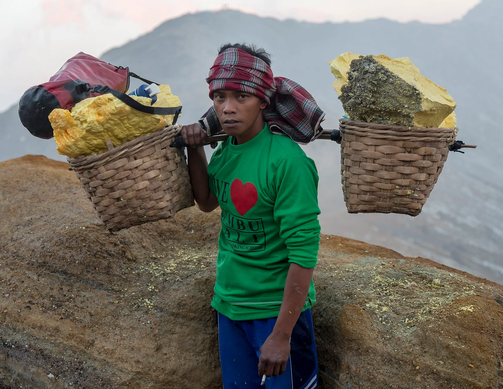 Seorang penambang belerang berjalan di jalur Kawah Ijen dengan keranjang di pundaknya.